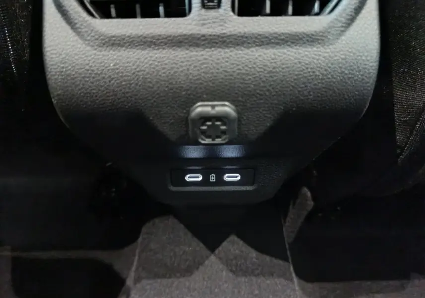 Vue rapprochée des ports USB-C arrière illuminés sur la console centrale noire du Dacia Bigster gris foncé.