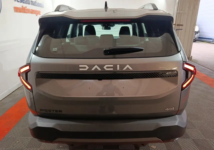 Vue arrière du Dacia Bigster gris foncé 4x4 avec feux LED allumés dans un garage intérieur.