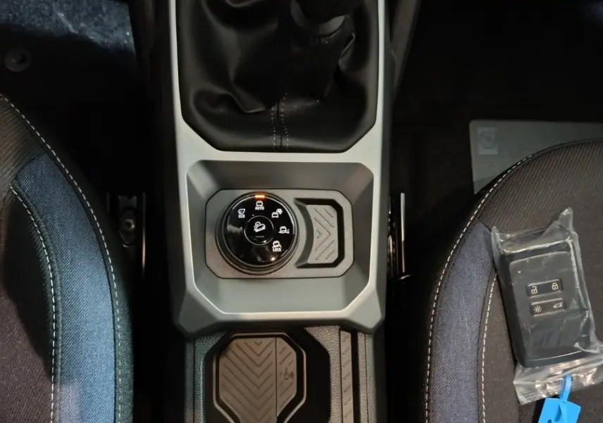 Vue plongeante sur la console centrale grise du Dacia Bigster 2025 avec levier de vitesse manuel et clé posée sur siège tissu bleu.