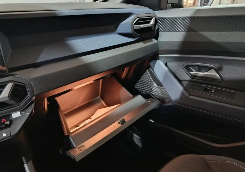 Vue intérieure côté passager du tableau de bord gris foncé du Dacia Bigster 2025 avec boîte à gants ouverte et porte de portière visible.