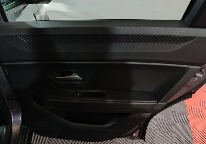 Vue intérieure côté gauche de la porte avant grise foncée du Dacia Bigster avec poignée et commande de vitre électrique.