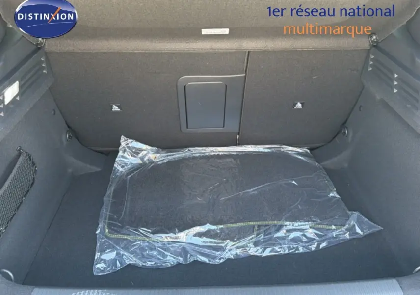 Coffre ouvert de la Peugeot 308 Hybrid 145ch GT noir perle métal, montrant un tapis de sol emballé en plastique.