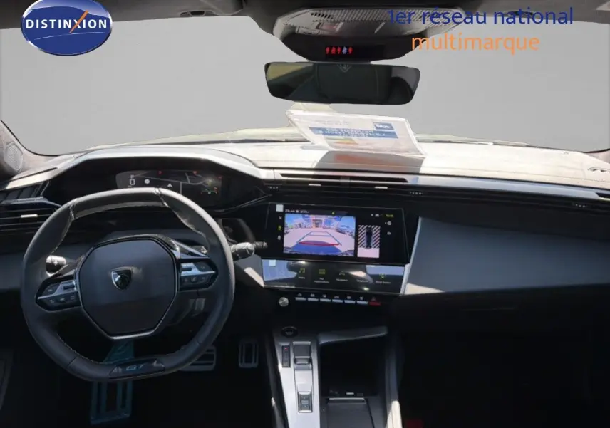 Vue intérieure du tableau de bord et volant noir de la Peugeot 308 Hybrid 145ch GT avec écran tactile et caméra de recul affichée.