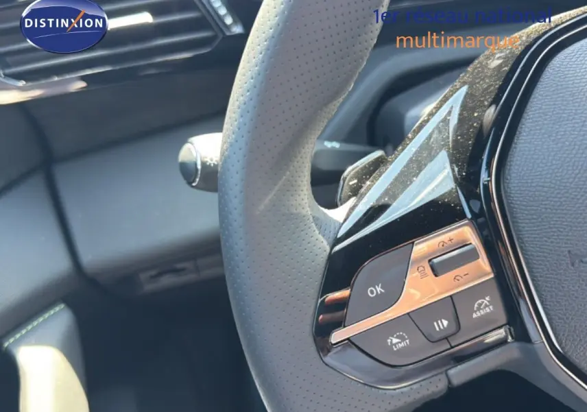 Gros plan sur le volant perforé gris clair de la Peugeot 308 Hybrid 145ch GT avec commandes intégrées et finition noire brillante.
