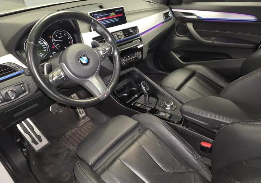 Intérieur noir cuir du BMW X2 M Sport 2023, vue côté conducteur avec volant M et éclairage d'ambiance violet.