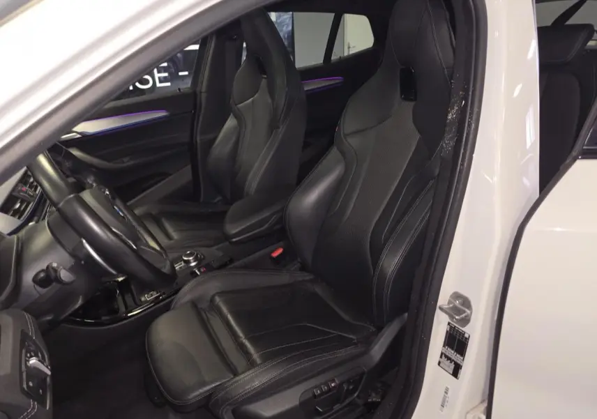 Vue intérieure côté gauche d'une BMW X2 blanche 2023 avec sièges sport M en cuir noir et éclairage d'ambiance violet.