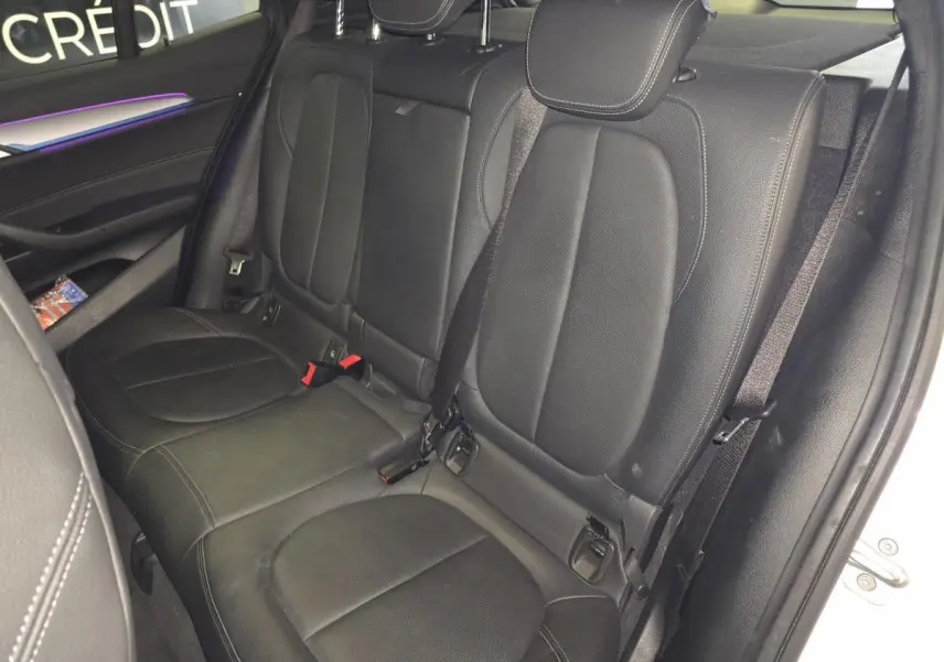 Vue intérieure arrière droite montrant la banquette en cuir noir perforé du BMW X2 sDrive18d M Sport blanc.