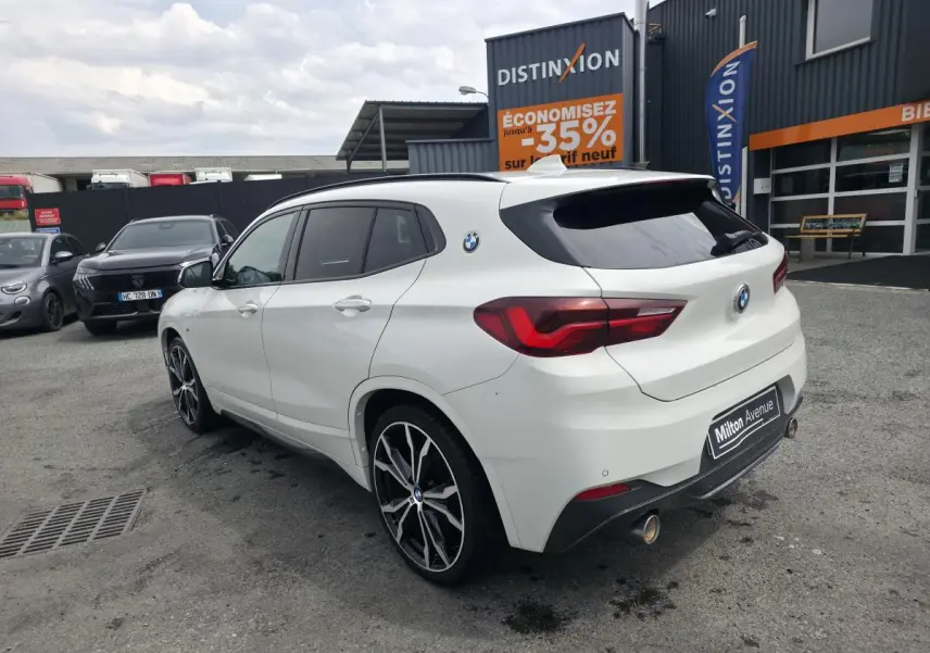BMW X2 sDrive 18d blanc vue 3/4 arrière droit, jantes alliage 20'' style M Sport et double sortie d’échappement chromée.