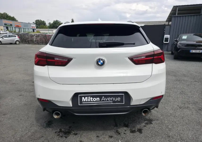 Vue arrière d'une BMW X2 sDrive 18d blanche avec double sortie d'échappement et feux arrière LED rouges.