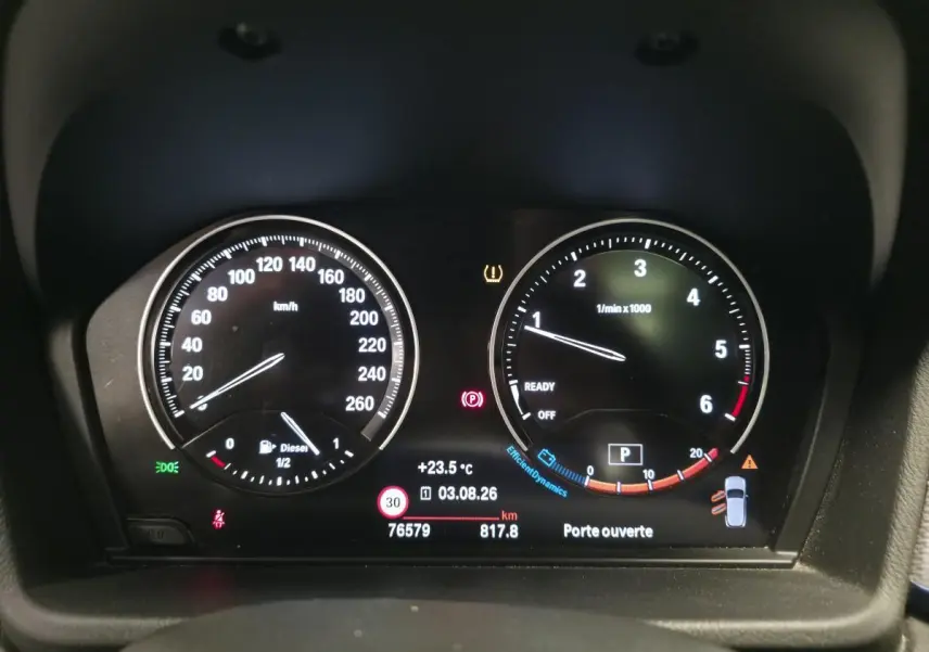 Tableau de bord numérique BMW X2 sDrive 18d 2023 affichant vitesse, régime moteur et alertes, vue frontale intérieure.