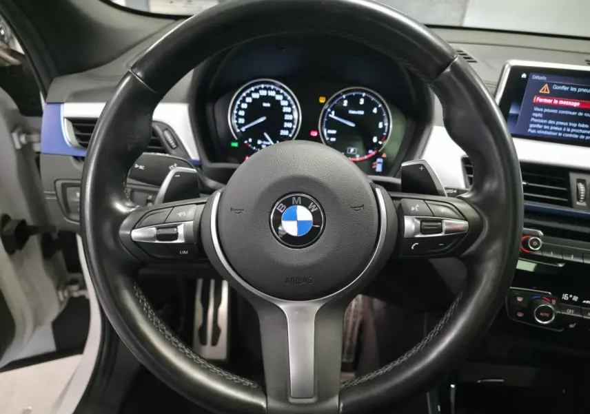 Vue rapprochée du volant cuir M noir avec commandes multifonctions et tableau de bord digital du BMW X2 blanc 2023.