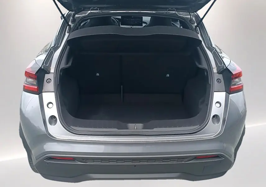 Vue arrière du coffre ouvert d'un Nissan Juke gris 2025, mettant en valeur l'espace de chargement et les feux arrière LED.