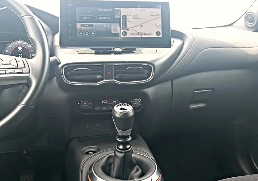 Vue intérieure centrée sur la console centrale et levier de vitesse manuel du Nissan Juke gris avec écran tactile et volant cuir.