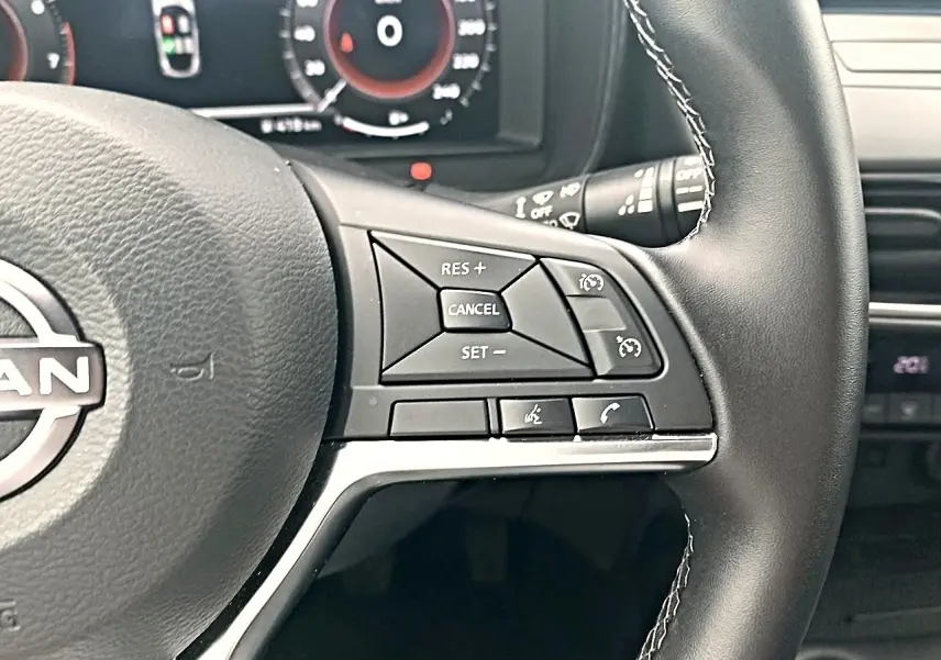 Gros plan sur les commandes multifonctions à droite du volant cuir noir du Nissan Juke gris 2025, tableau de bord en arrière-plan.