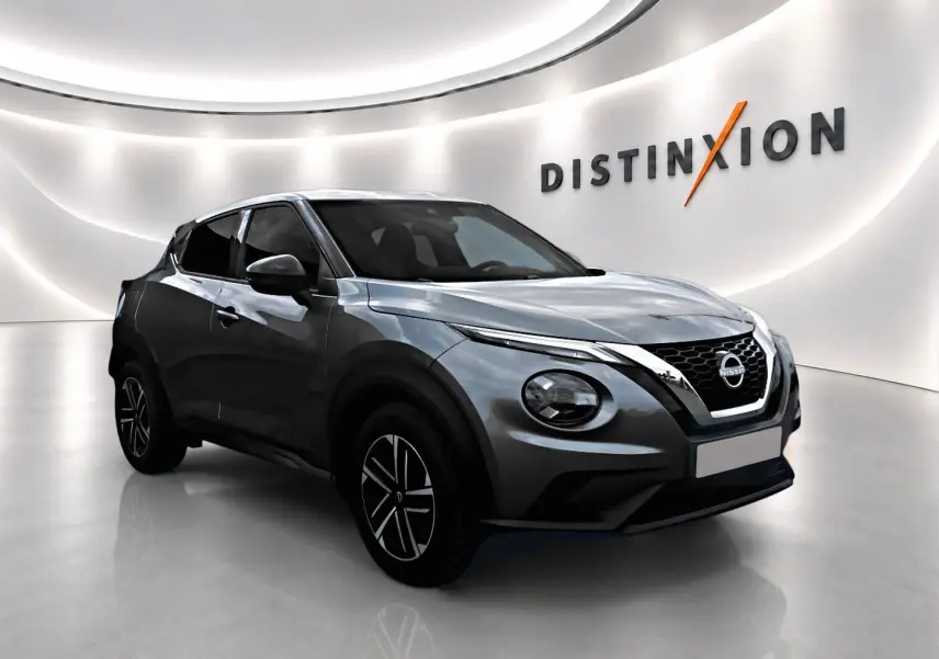 Nissan Juke gris en 3/4 avant droit dans un showroom lumineux avec jantes alliage et calandre chromée.