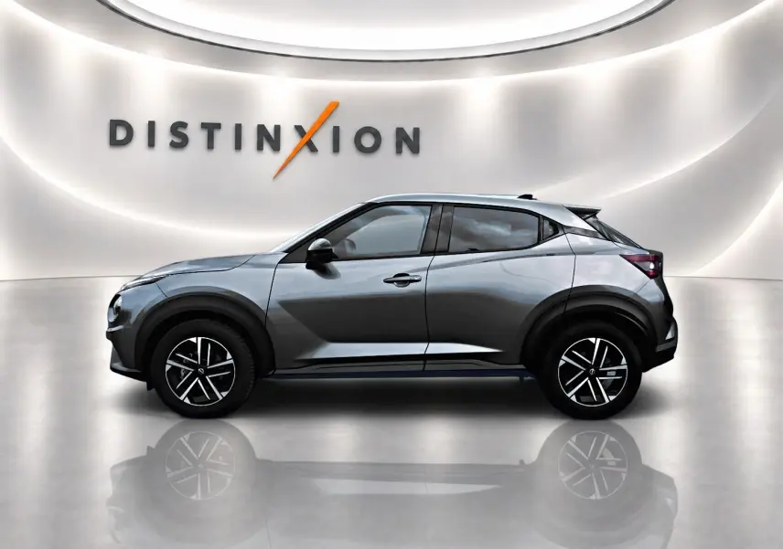 Profil droit d'un Nissan Juke 2025 gris avec jantes alliage noires, dans un showroom lumineux au mur blanc.