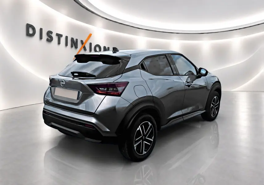 Vue 3/4 arrière droite du Nissan Juke gris 2025 avec jantes alliage et toit noir contrasté dans un showroom.