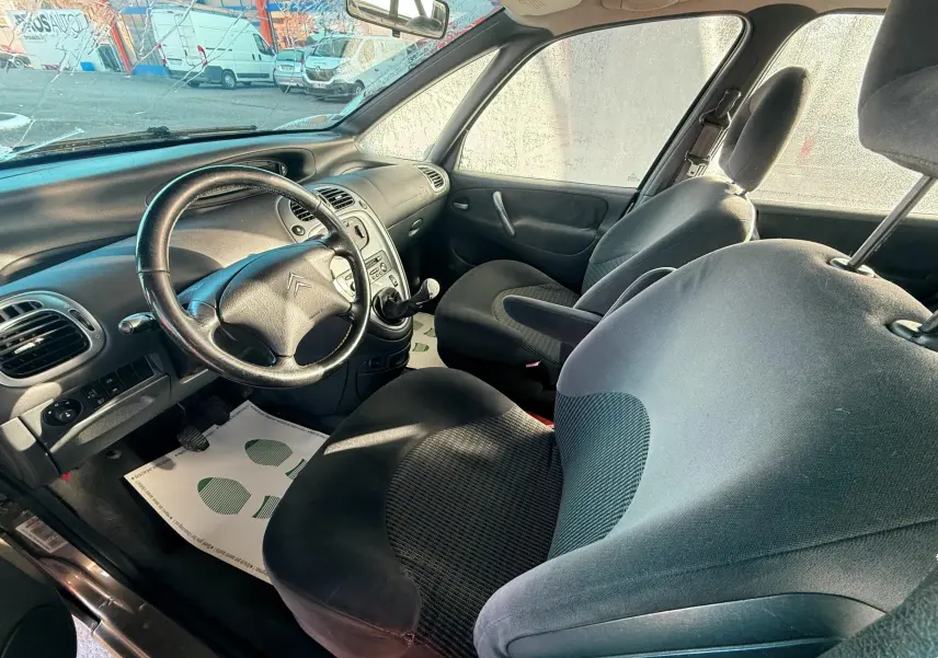 Vue intérieure avant droite du Citroën Xsara Picasso 2009, montrant le volant cuir et les sièges tissu noir.