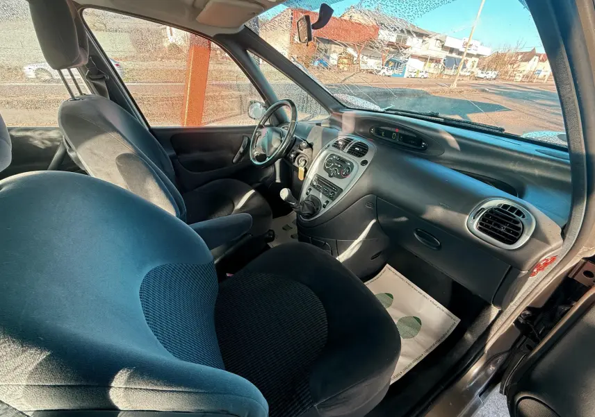 Vue intérieure côté passager du tableau de bord et des sièges noirs d'une Citroën Xsara Picasso beige de 2009.