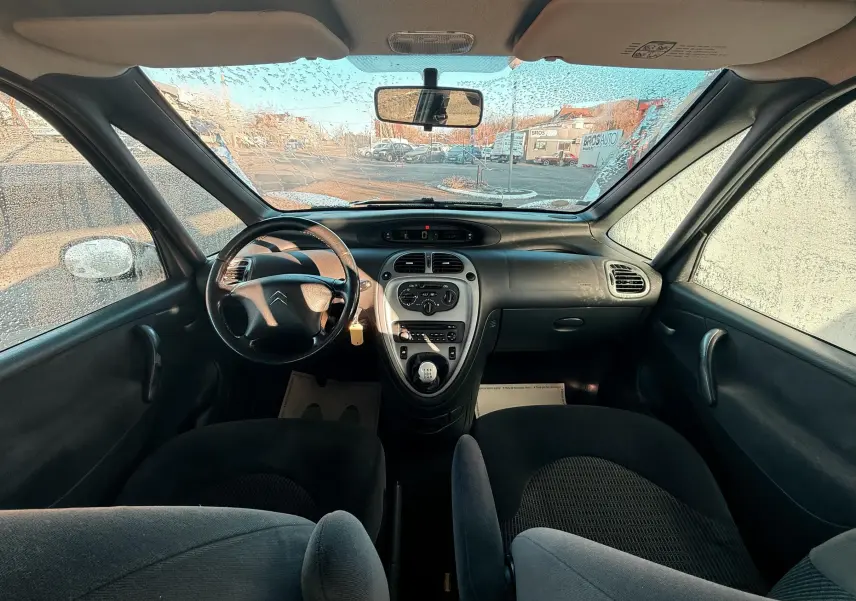 Vue intérieure avant du Citroën Xsara Picasso 2009, tableau de bord noir avec volant cuir et levier de vitesse manuel.