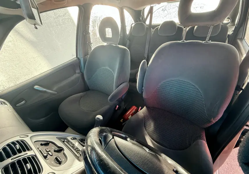 Vue intérieure avant droite de la Citroën Xsara Picasso avec sièges noirs et volant en cuir visible.