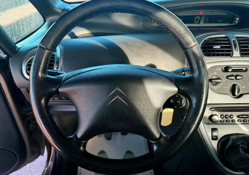 Vue rapprochée du volant en cuir noir d’une Citroën Xsara Picasso 2009, avec tableau de bord et commandes visibles.