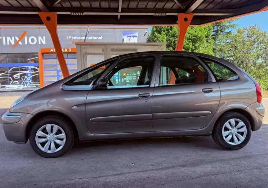 Vue de profil côté gauche d'une Citroën Xsara Picasso beige de 2009 stationnée sous un abri.
