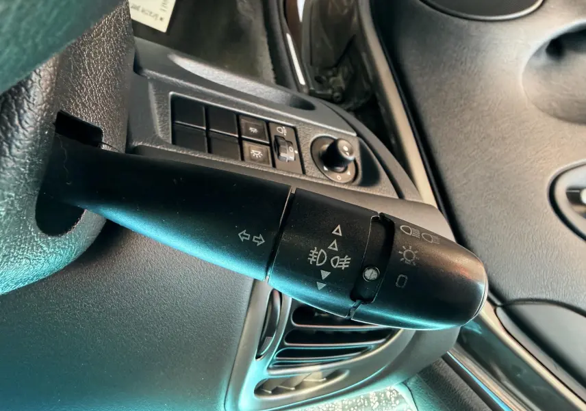 Gros plan sur la commande des feux et clignotants côté gauche du tableau de bord intérieur d'une Citroën Xsara Picasso beige.