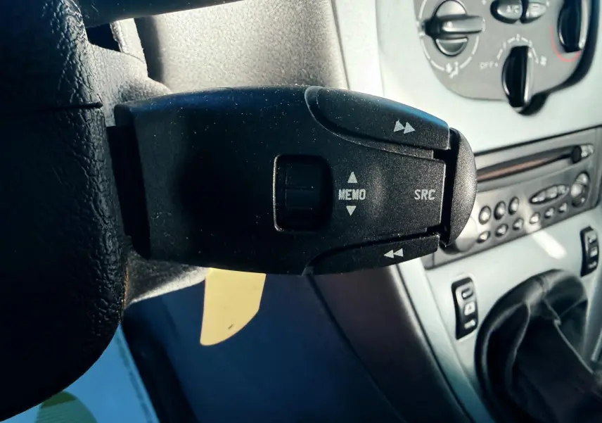 Gros plan sur la commande au volant noire de la Citroën Xsara Picasso beige, avec tableau de bord et levier de vitesses visibles.