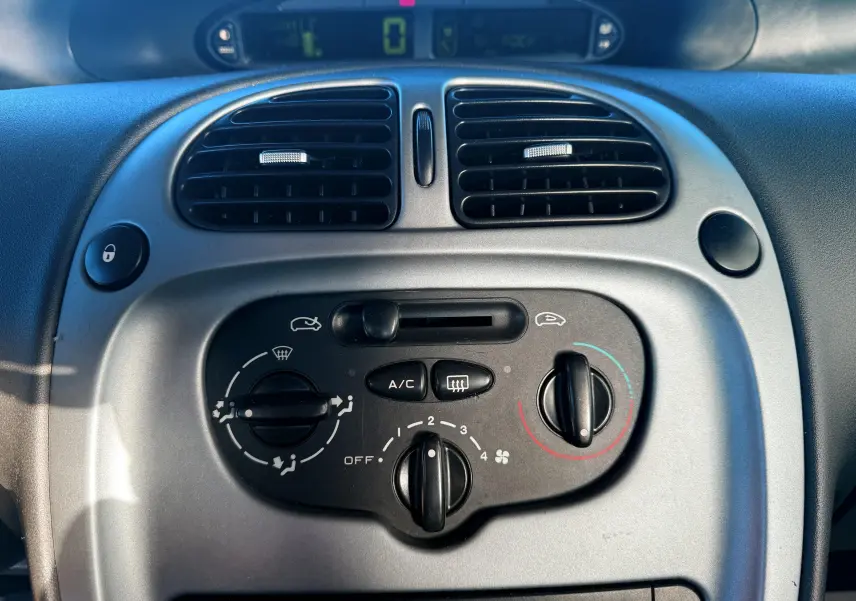 Vue rapprochée du tableau de bord gris avec commandes de climatisation et aérateurs noirs du Citroën Xsara Picasso.