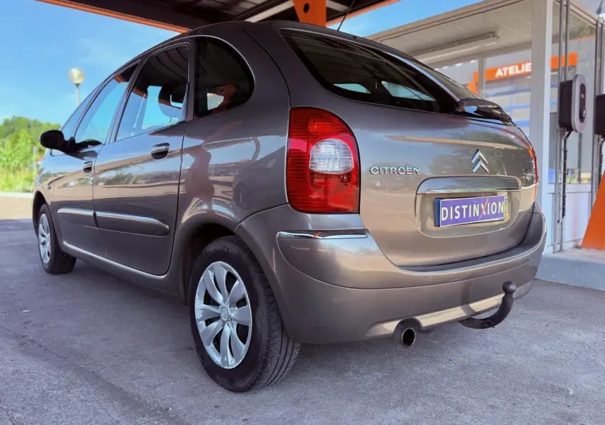Vue 3/4 arrière droite d'une Citroën Xsara Picasso beige de 2009 avec attelage sous un auvent.