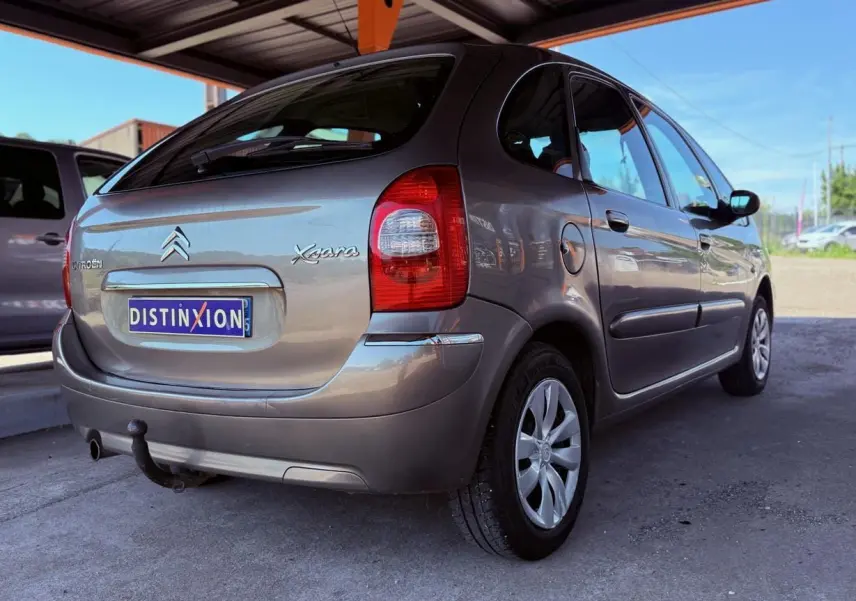 Vue 3/4 arrière droite d'une Citroën Xsara Picasso beige 2009 avec attelage sous un abri.