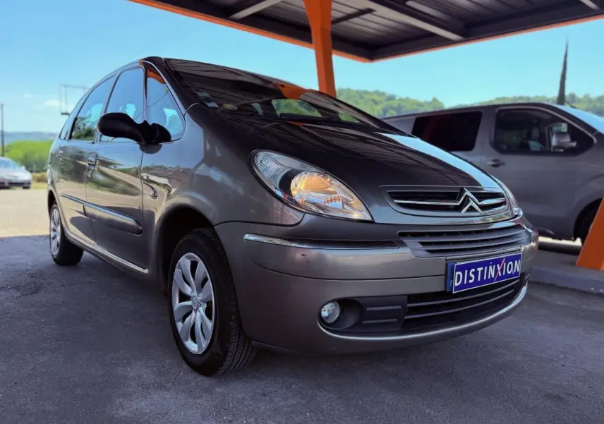 Citroën Xsara Picasso beige vue 3/4 avant droit sous un abri avec plaque Distinxion visible.