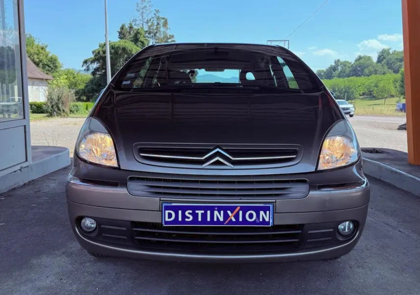 Vue avant d'une Citroën Xsara Picasso beige de 2009 avec phares allumés et plaque Distinxion visible.