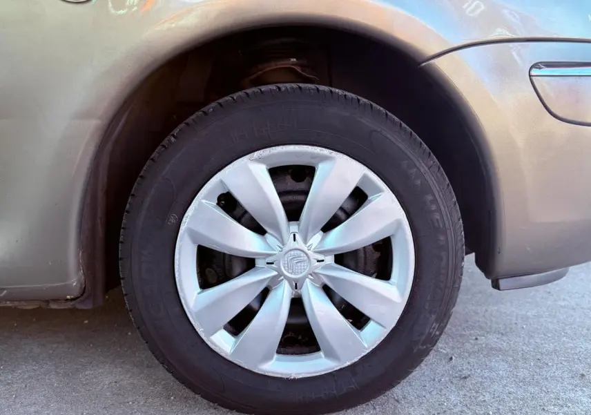 Gros plan sur la roue avant droite beige d'une Citroën Xsara Picasso avec enjoliveur argenté en extérieur.