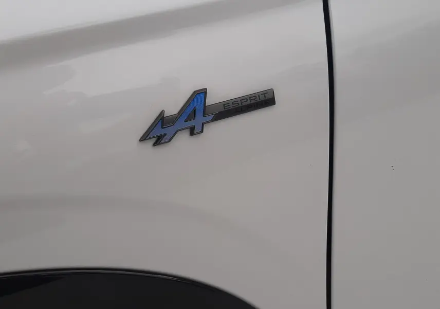 Gros plan sur l'écusson Esprit Alpine bleu et noir sur la portière blanche nacrée du Renault Austral.