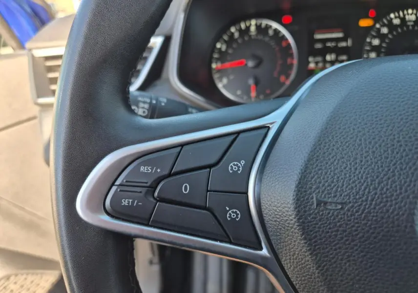 Gros plan sur le volant de la Renault Clio bleu foncé 2023, montrant les commandes du régulateur de vitesse côté gauche.