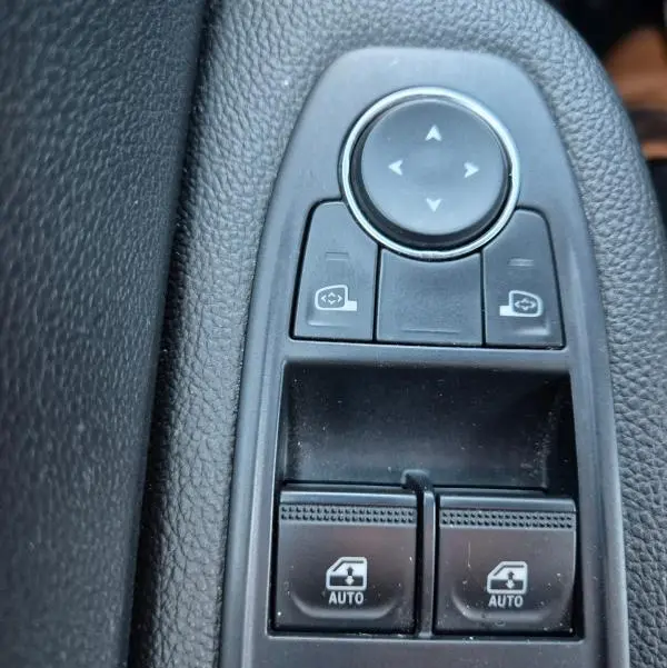 Gros plan sur les commandes de lève-vitres et réglage des rétroviseurs intérieurs d'une Renault Clio bleu foncé 2023.