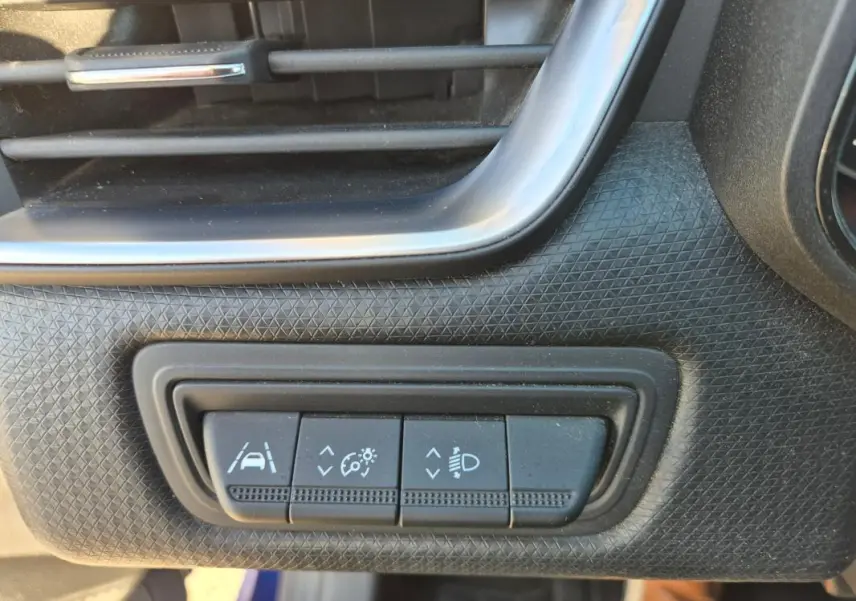 Détail intérieur montrant les commandes d'assistance à la conduite sur tableau de bord noir d'une Renault Clio bleu foncé.