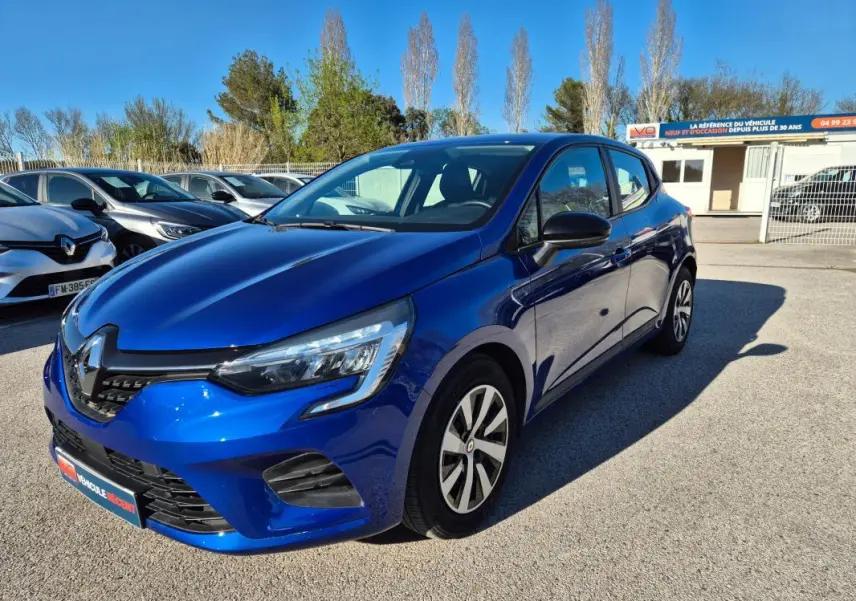 Renault Clio V TCe 90 bleu foncé vue 3/4 avant droit sur parking ensoleillé avec calandre noire distinctive.