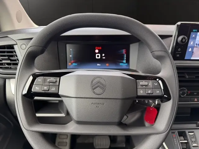 Vue rapprochée du volant multifonctions noir du Citroën Jumpy blanc, avec tableau de bord numérique en arrière-plan.