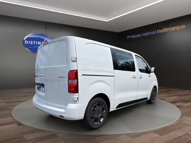 Vue 3/4 arrière droite d’un Citroën Jumpy blanc, fourgon utilitaire avec vitres latérales teintées et jantes noires.