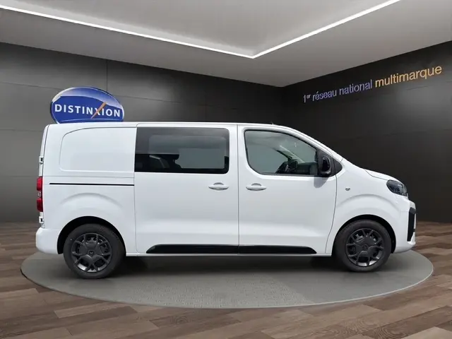Vue latérale droite d'un Citroën Jumpy blanc 2026 avec vitres teintées et jantes noires en exposition intérieure.