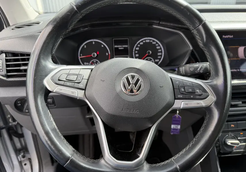 Vue rapprochée du volant en cuir noir du Volkswagen T-Cross gris 2019, avec commandes intégrées et tableau de bord visible.