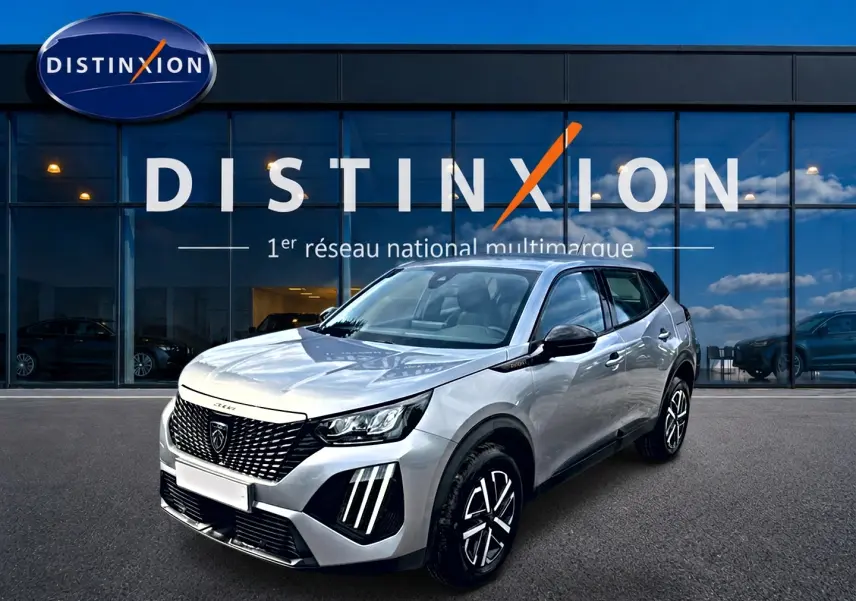 Peugeot 2008 gris en 3/4 avant droit, avec calandre noire et feux LED distinctifs, devant showroom Distinxion.