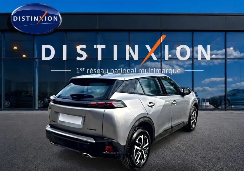 Peugeot 2008 gris en 3/4 arrière droit, avec becquet et feux arrière LED visibles devant un showroom Distinxion.