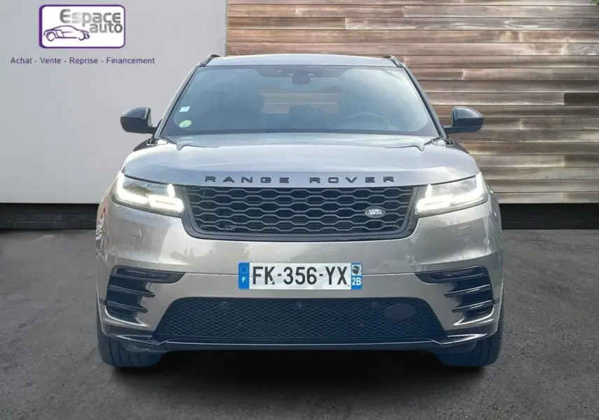 Vue frontale d'un Range Rover Velar gris 2019 avec calandre noire et phares LED allumés sur fond urbain.