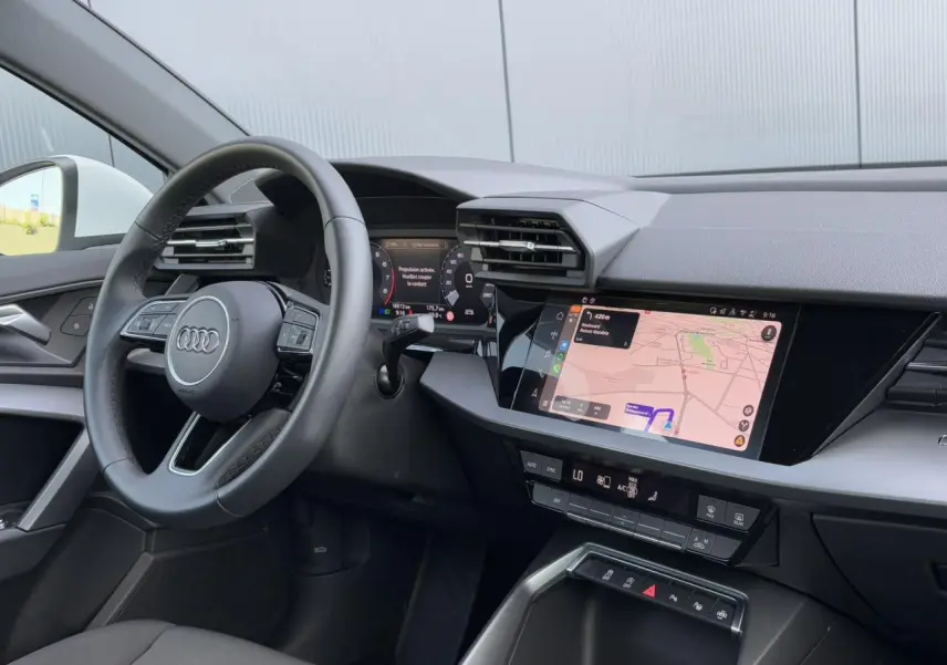 Intérieur Audi A3 Sportback 2024 vu côté gauche, tableau de bord noir avec écran tactile affichant la navigation.