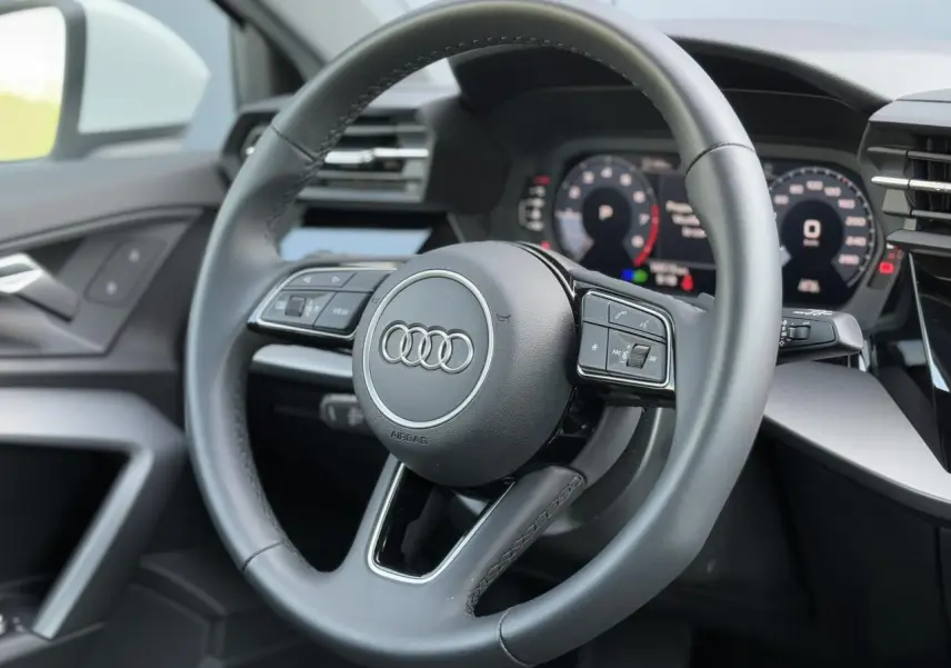 Volant cuir 3 branches multifonctions de l'Audi A3 Sportback 2024, vue rapprochée du poste de conduite intérieur.