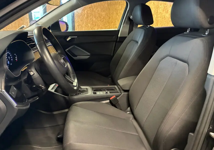 Vue intérieure côté conducteur de l'Audi Q3 Sportback noir, avec sièges en tissu et volant multifonctions cuir.